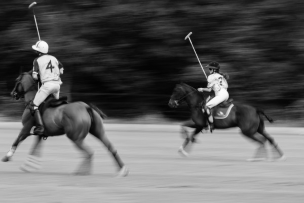 Two teens ride polo ponies across a field.