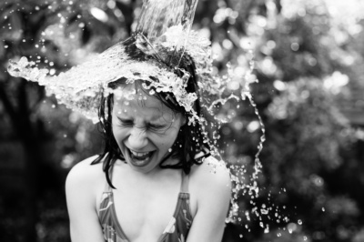 Water tips onto a girls head in summer garden fun.