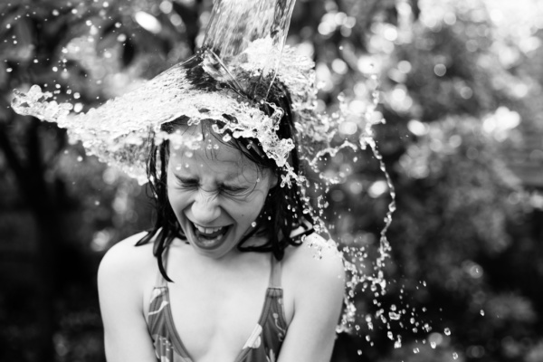 Water tips onto a girls head in summer garden fun.