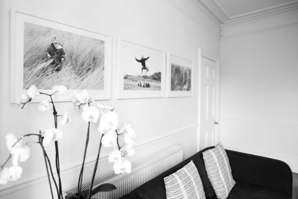 Family portraits in white tulip wooden frames displayed over the top of a sofa.