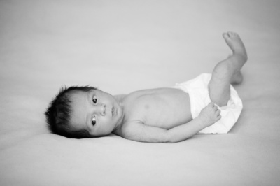 A wide-eyed newborn kicks their feet while on a bed.