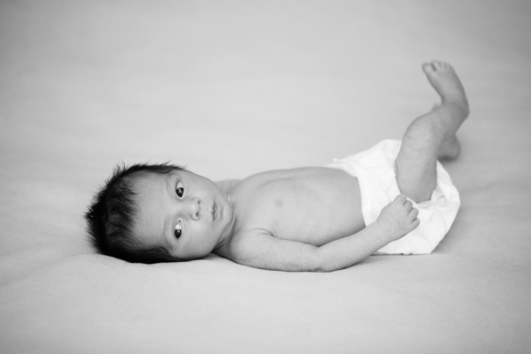 A wide-eyed newborn kicks their feet while on a bed.