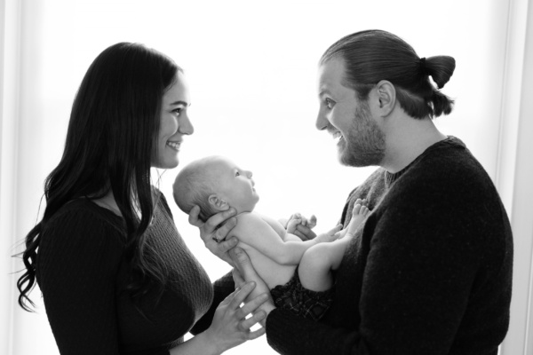 A window frames parents and their newborn.