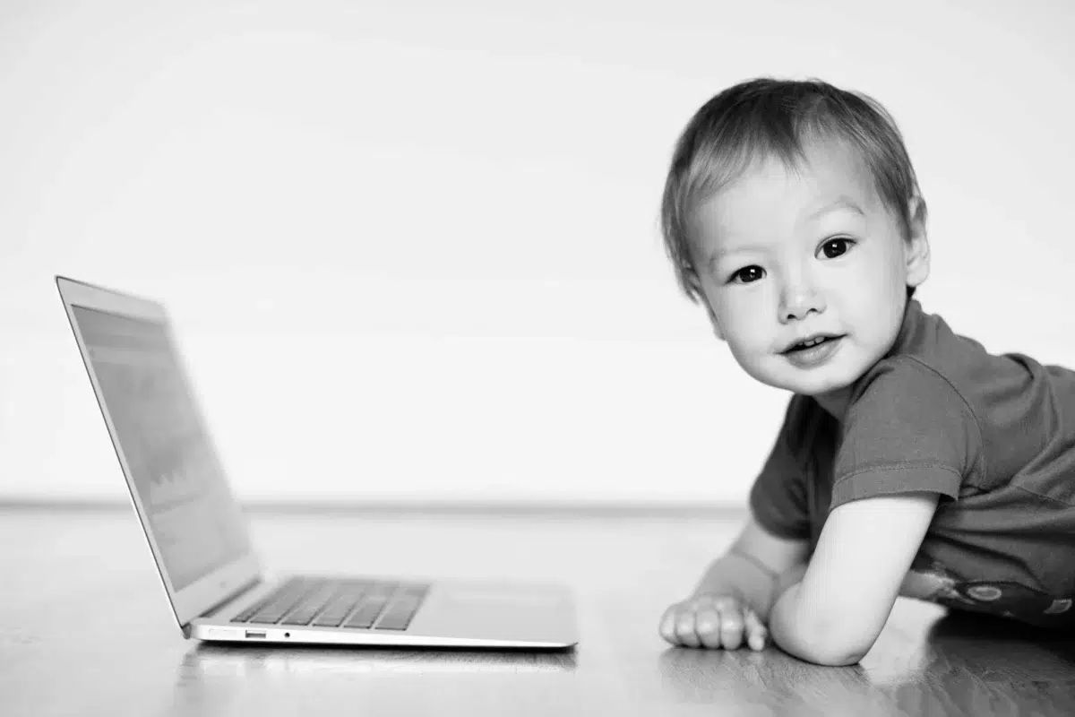 child smiles at the camera while playing with a mac laptop.