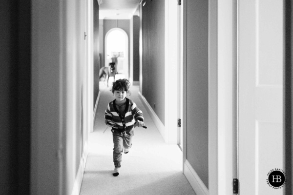 little-boy-runs-down-corridor-at-home-on-family-photo-shoot