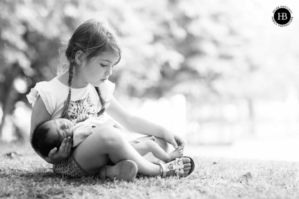 newborn-baby-held-older-sister-outdoors