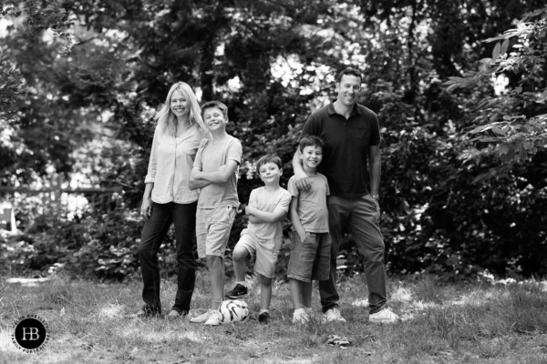 Family of five smiling together in a woodland clearing during a summer photo session.
