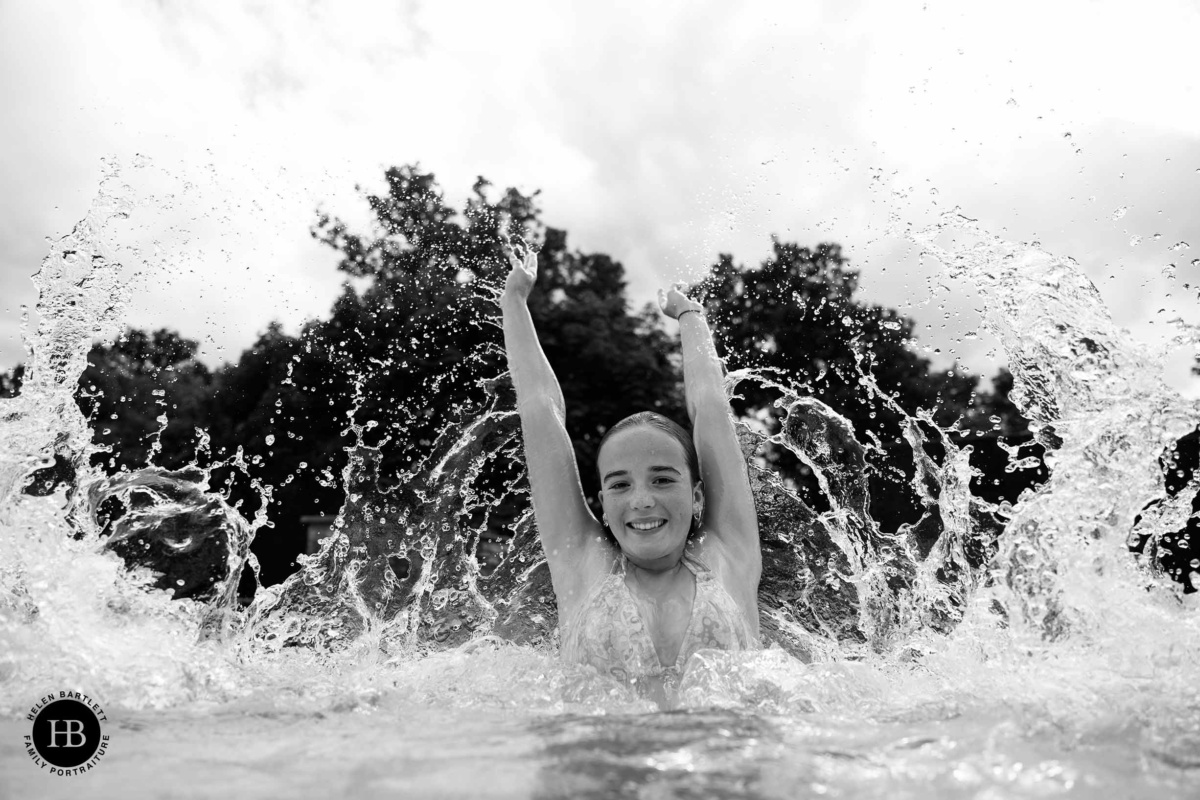 Teenage girl splashing water with arms raised in swimming pool