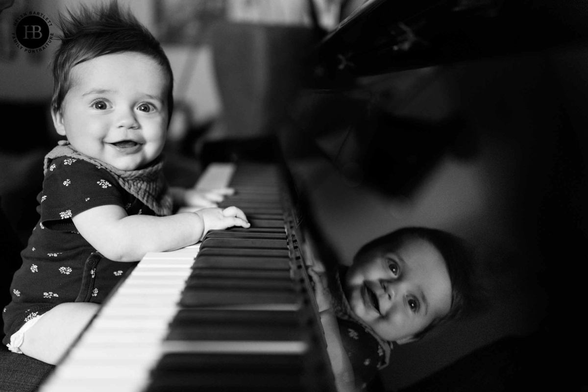 Smiling baby sitting at piano keys with reflection in the glossy surface.