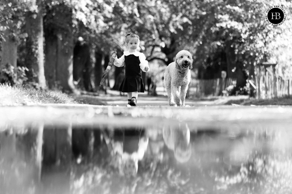 Young girl walks beside a fluffy dog while holding a small umbrella during a family photo shoot at Morden Hall in South London.