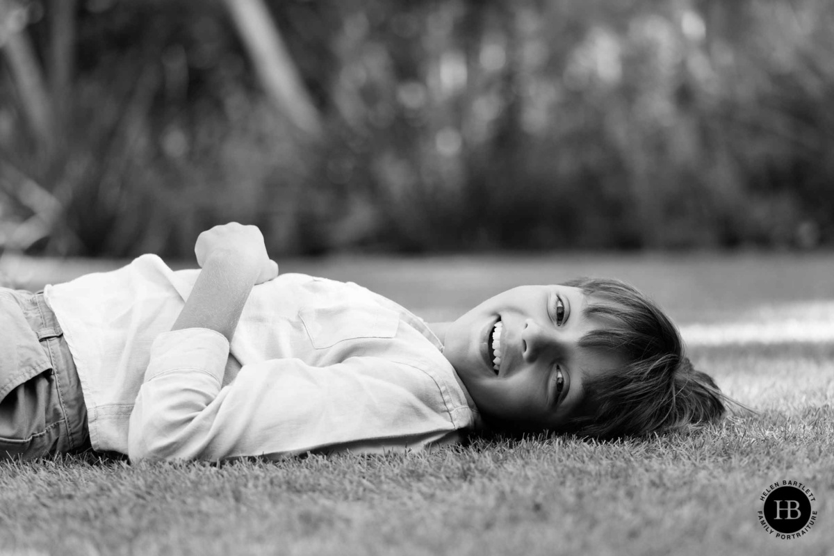 Boy lying on grass outdoors smiling during family photo shoot in Wimbledon