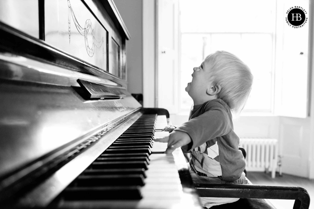 Toddler standing on a piano stool, reaching for the keys in a bright living room