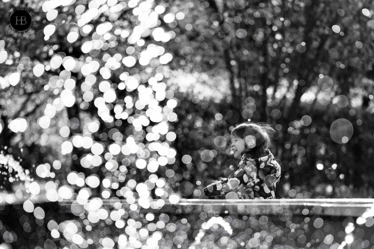 Child playing near a fountain with soft background light during a family photo shoot