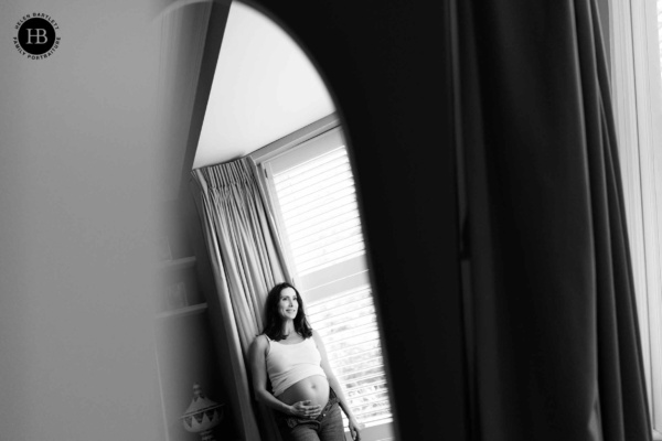 Pregnant woman standing by a window at home during a maternity photo shoot in Highgate