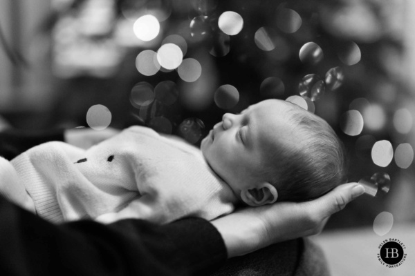 Sleeping newborn cradled in an adult’s hands with soft lights glowing in the background at home newborn photo shoot Highgate