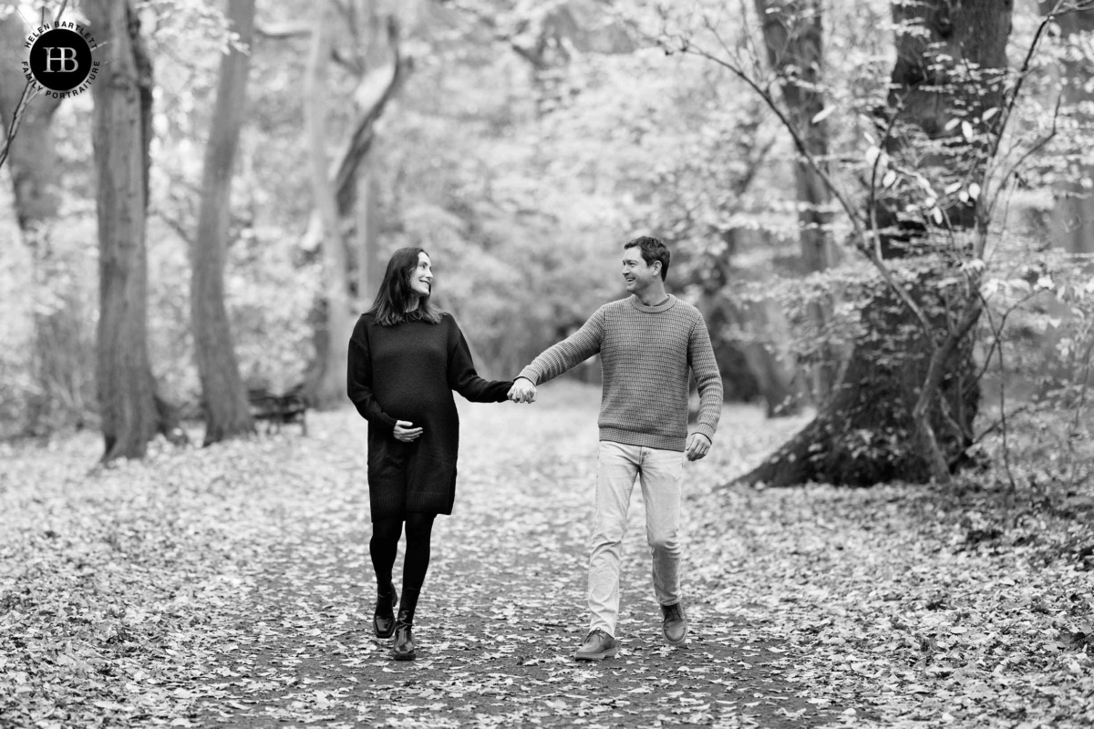 Expectant couple holding hands while walking through Highgate Wood
