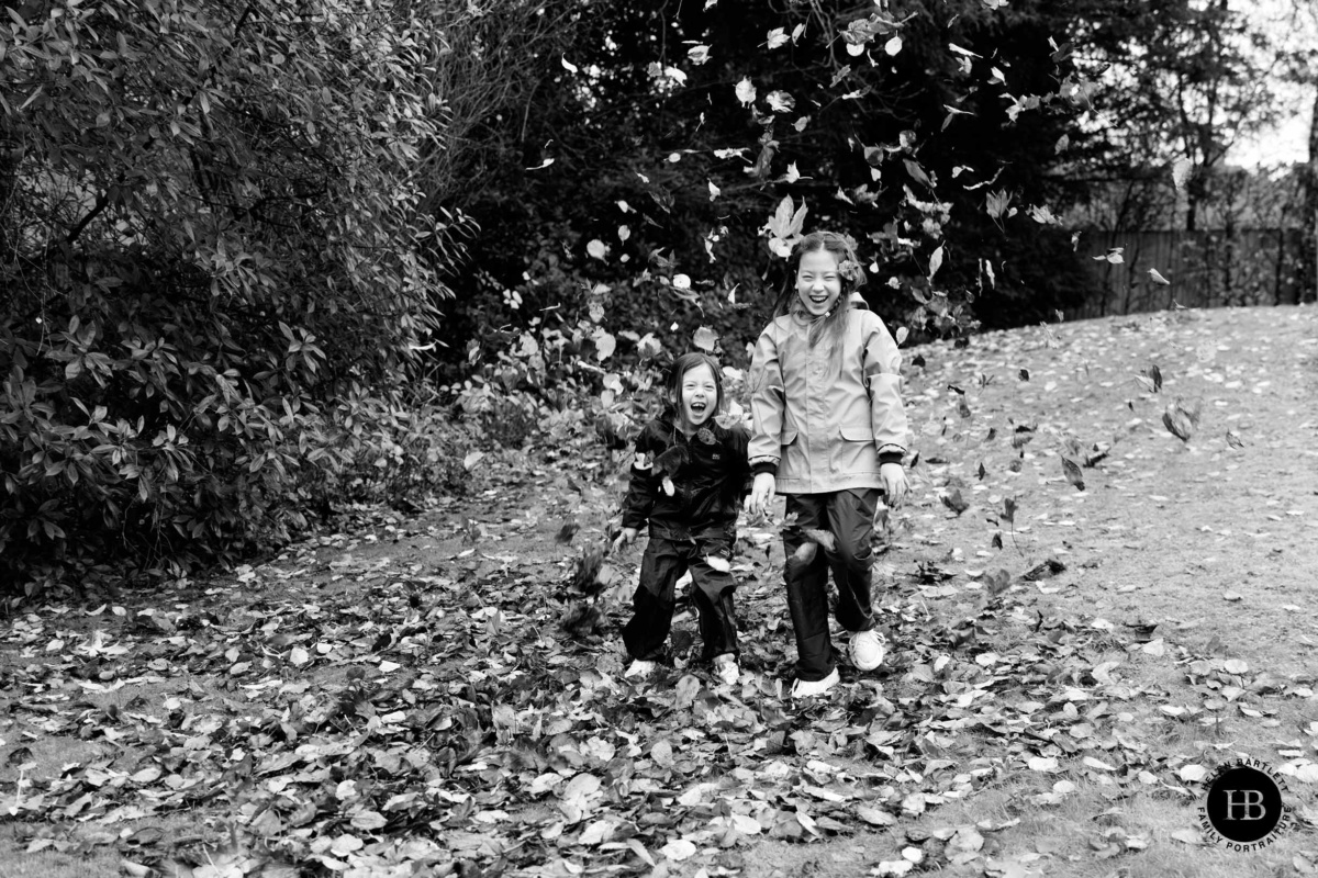 Two sisters laughing while running through autumn leaves on family photo shoot in Mill Hill