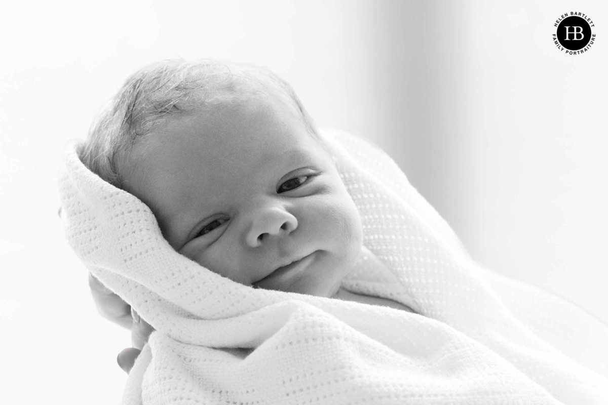 Awake newborn baby wrapped in a blanket and looking towards the camera during newborn photography in Queens Park