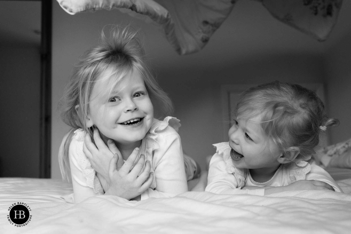 Two young girls laughing and playing under duvet during indoor family photo shoot