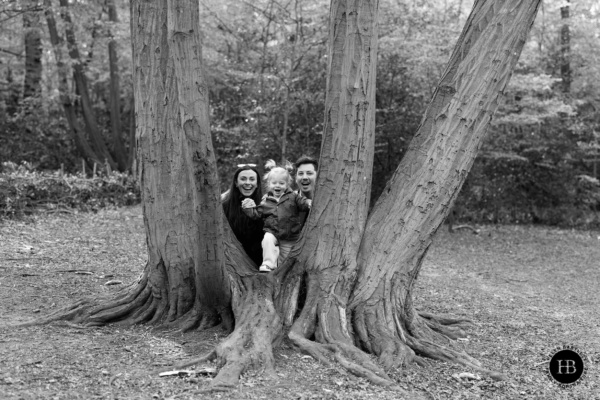 Family with toddler peeking through trees in Highgate Wood