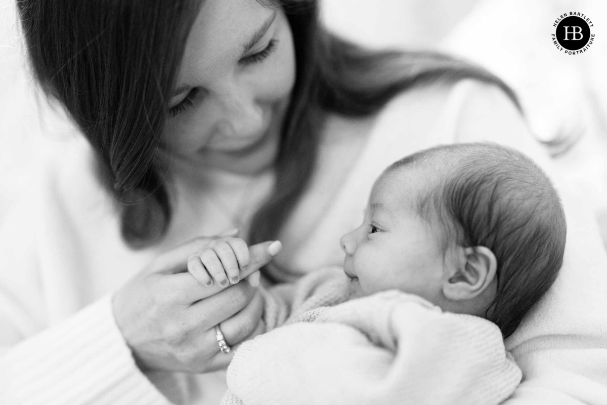 Mother holding newborn baby who is touching her finger during newborn photography Chiswick at home
