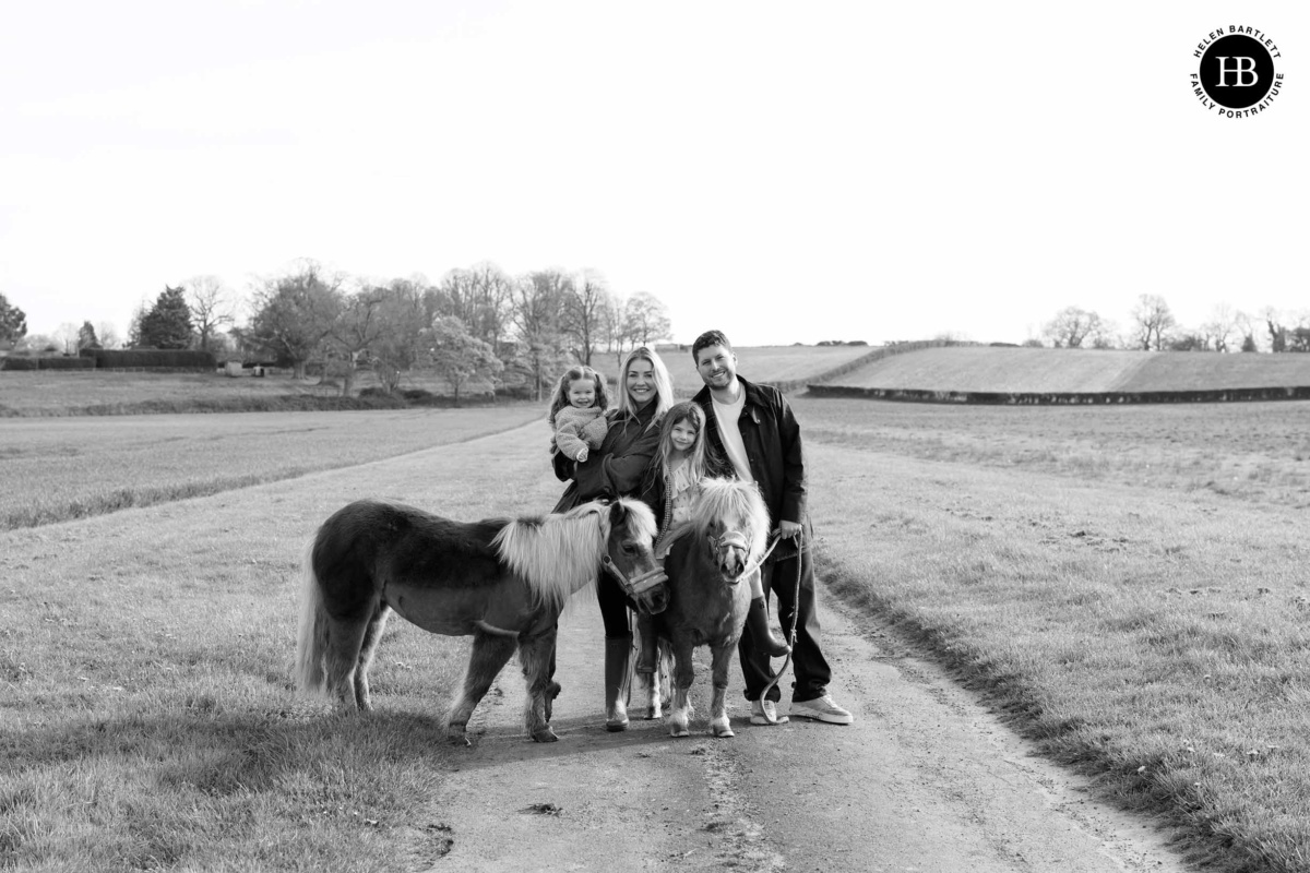 Family standing with ponies on a country path during a family photo shoot in Cranleigh
