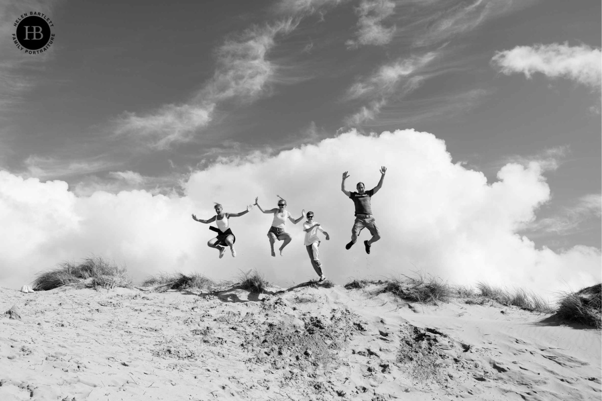 family leaps over a sand dune on a sunny family photography session with Helen Bartlett