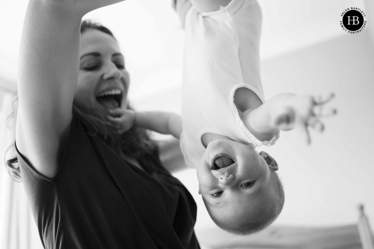 joyful mother and baby photograph as mother holds her daughter upside down. The baby is laughing and reaching for the camera.