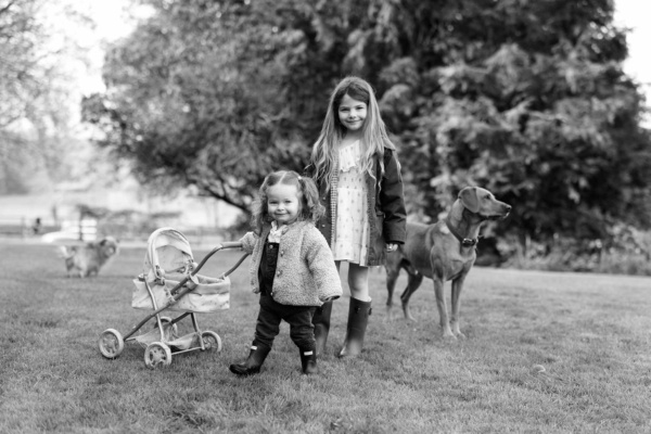 Two sisters standing with a toy buggy and dog during a family photo shoot in Cranleigh