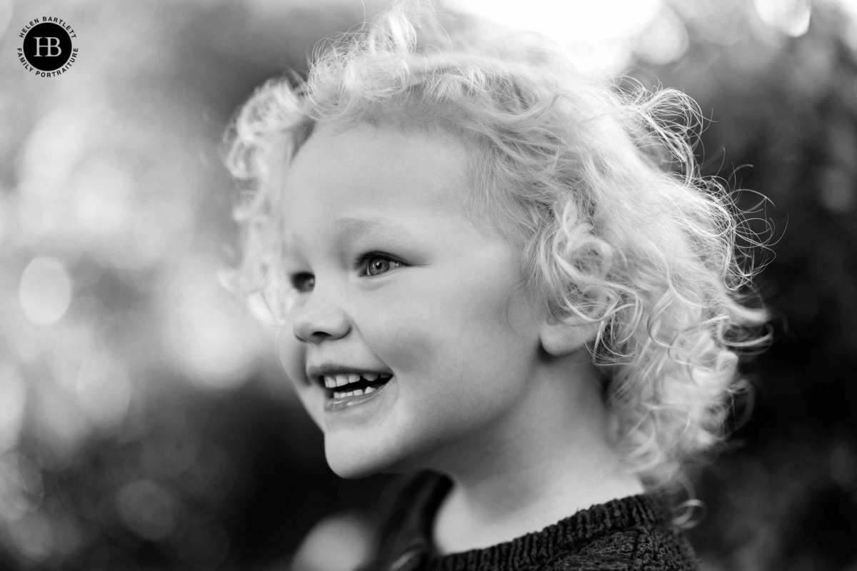 Close-up black and white portrait of a curly-haired toddler girl laughing outdoors