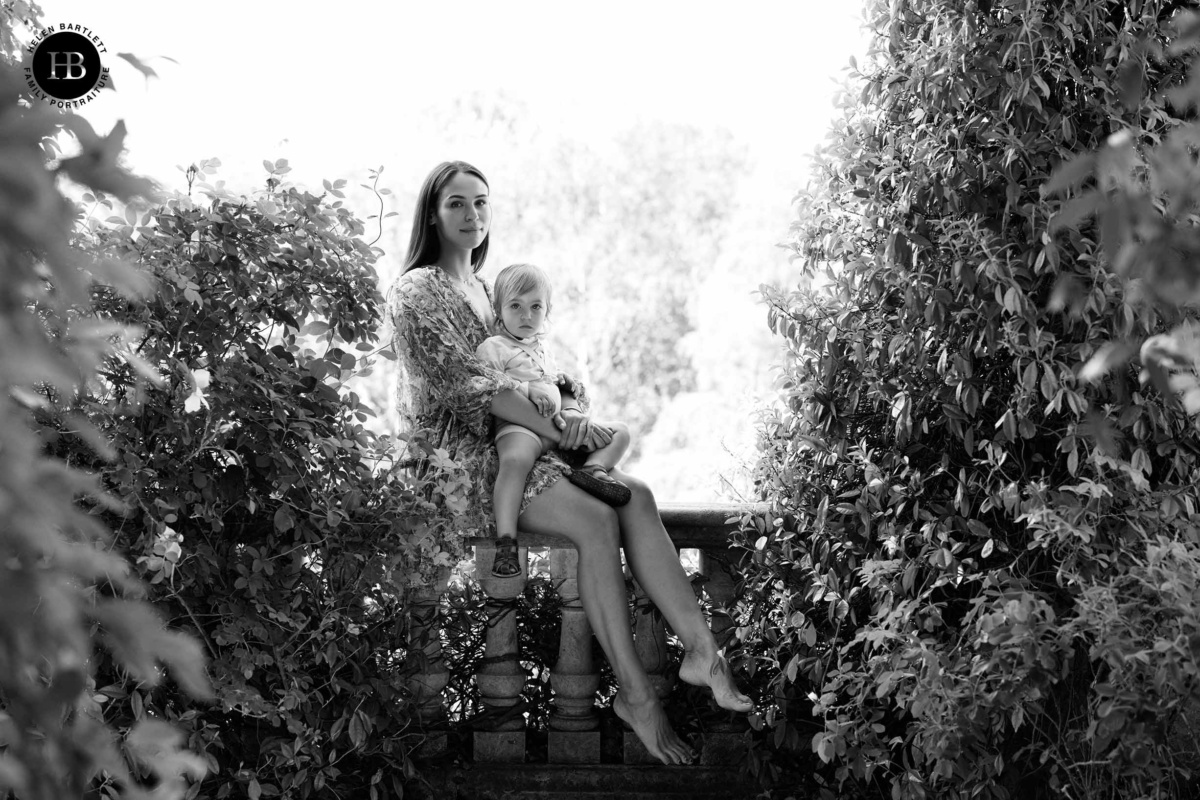 Mother and toddler son sitting together on stone balustrade at Hampstead Heath Pergola