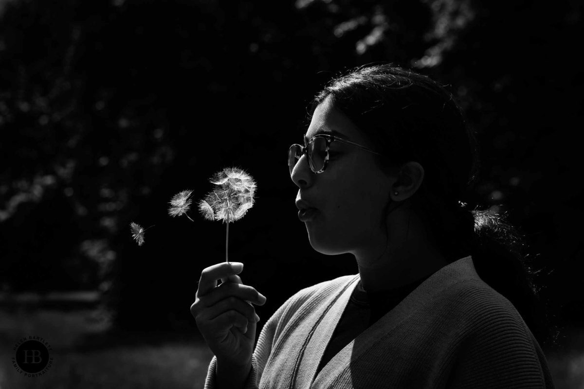 Backlit black and white portrait of a teenager blowing a dandelion clock in Hyde Park