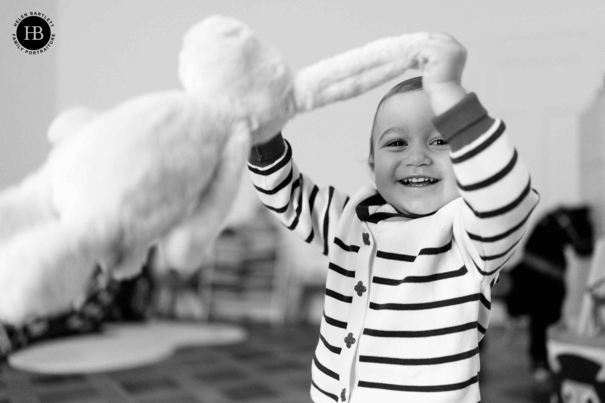 Toddler laughing as she swings a soft rabbit toy above her head