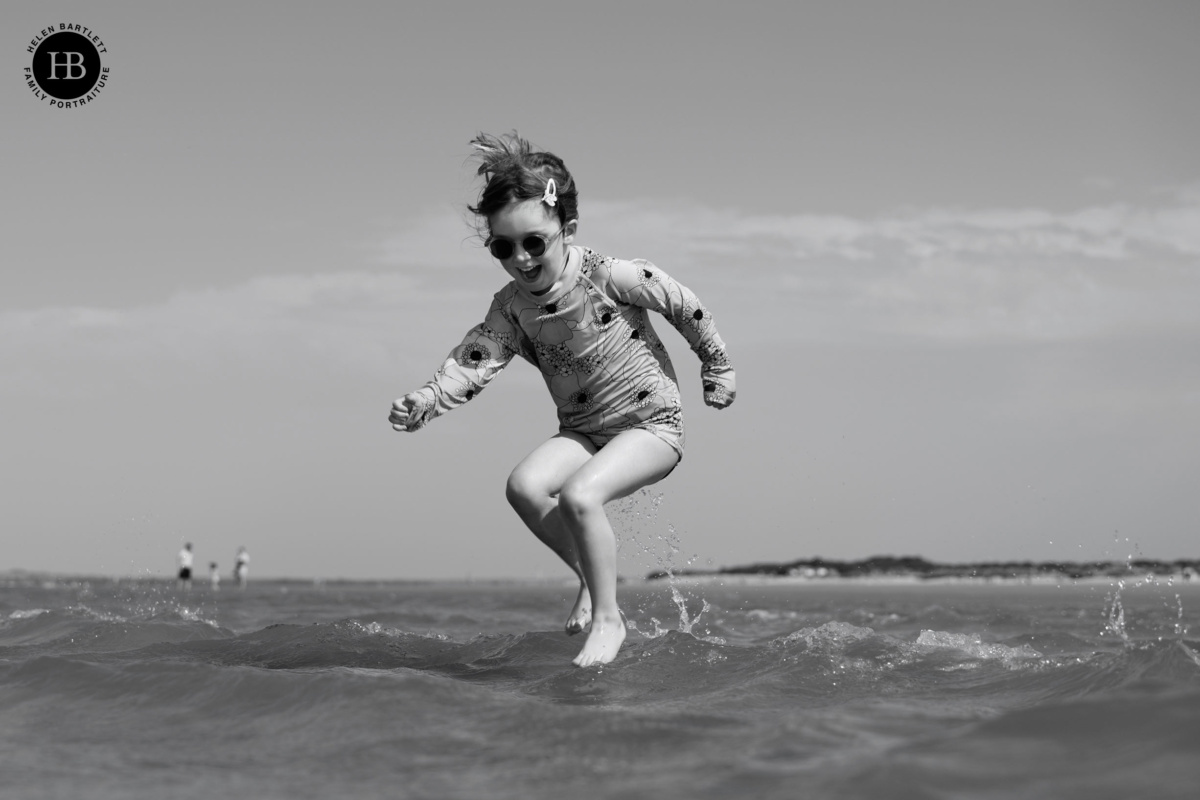 Girl in sunglasses jumping over a small wave at West Witterin