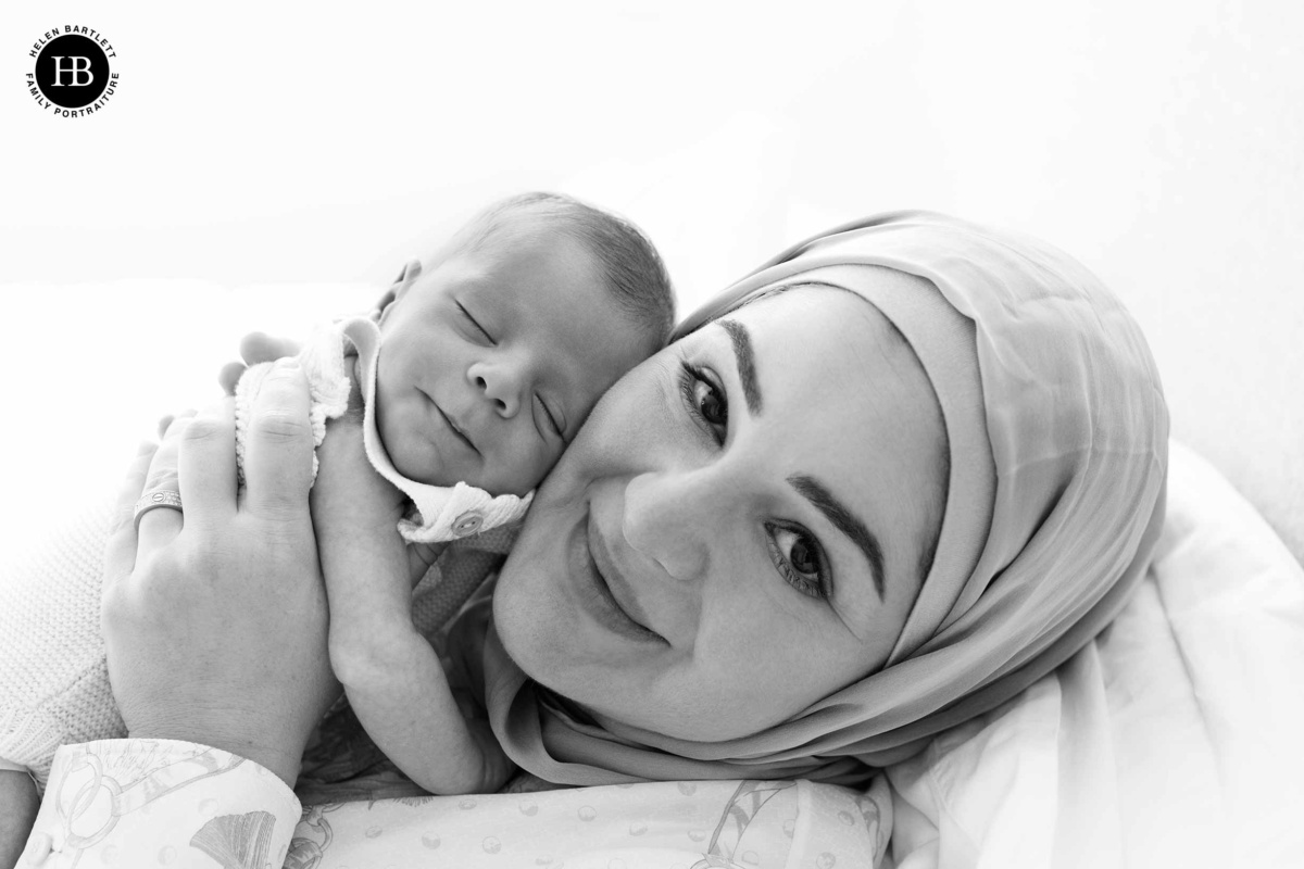 Close-up portrait of a mother resting cheek to cheek with her sleeping newborn son