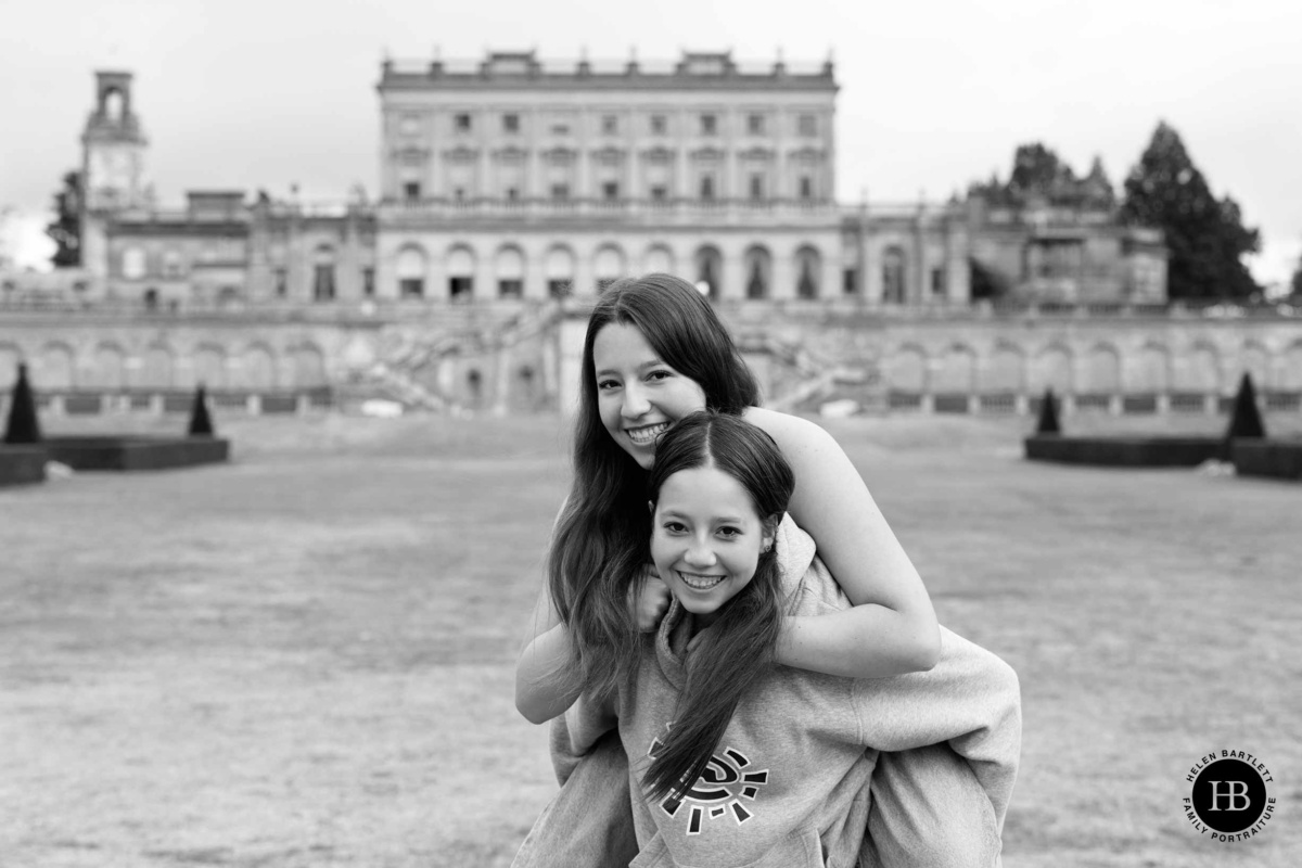 Teenage sisters laughing during a piggyback ride in front of Cliveden House