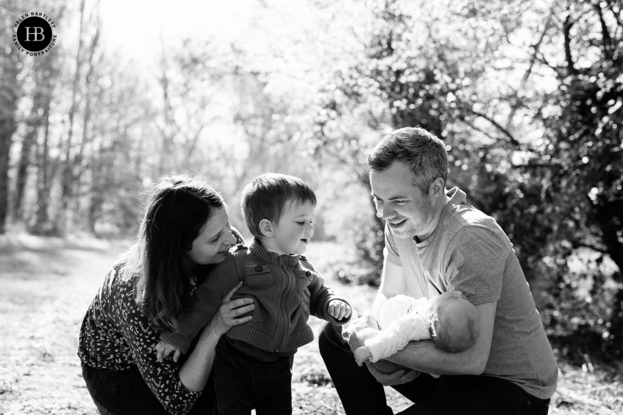 dad cradles newborn baby as mum and toddler look on in charming family photograph in North London