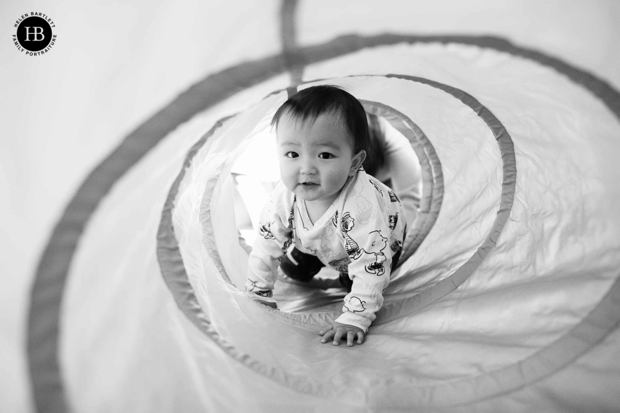 one year old baby crawls through fabric tunnel during an at-home baby photo shoot