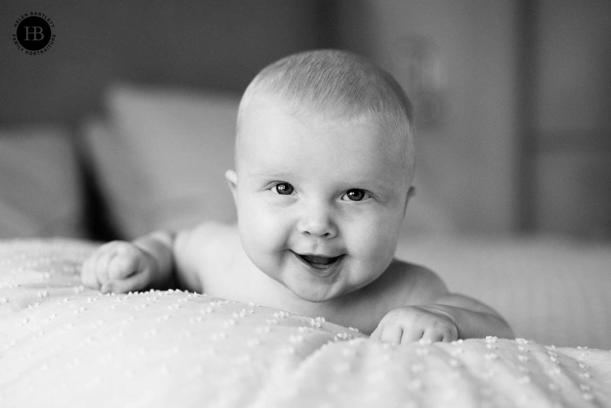 baby lies on tummy on bed laughing at camera, professional baby photograph taken at clients home in Islington