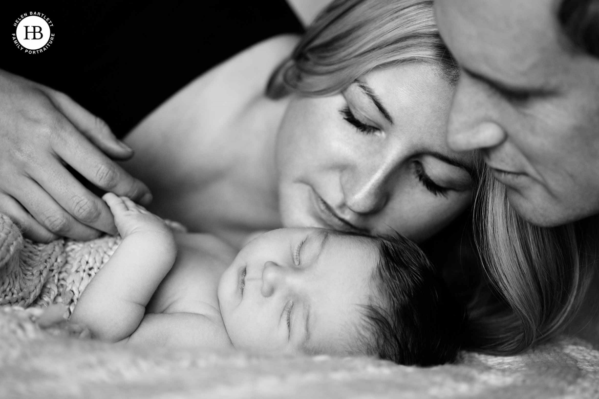 mum and dad snuggle with sleeping newborn in professional photo