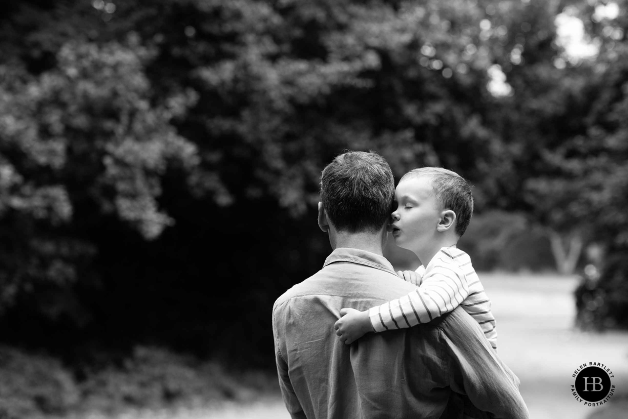 tired four year old boy sleeps on dad's shoulder on Hampstead Heath