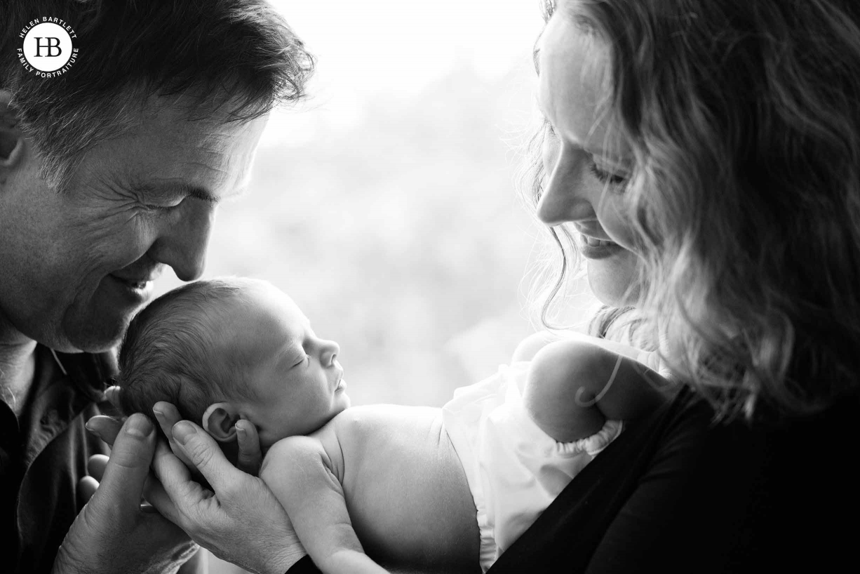 Dad kisses baby's head as mum looks on in black and white family photo