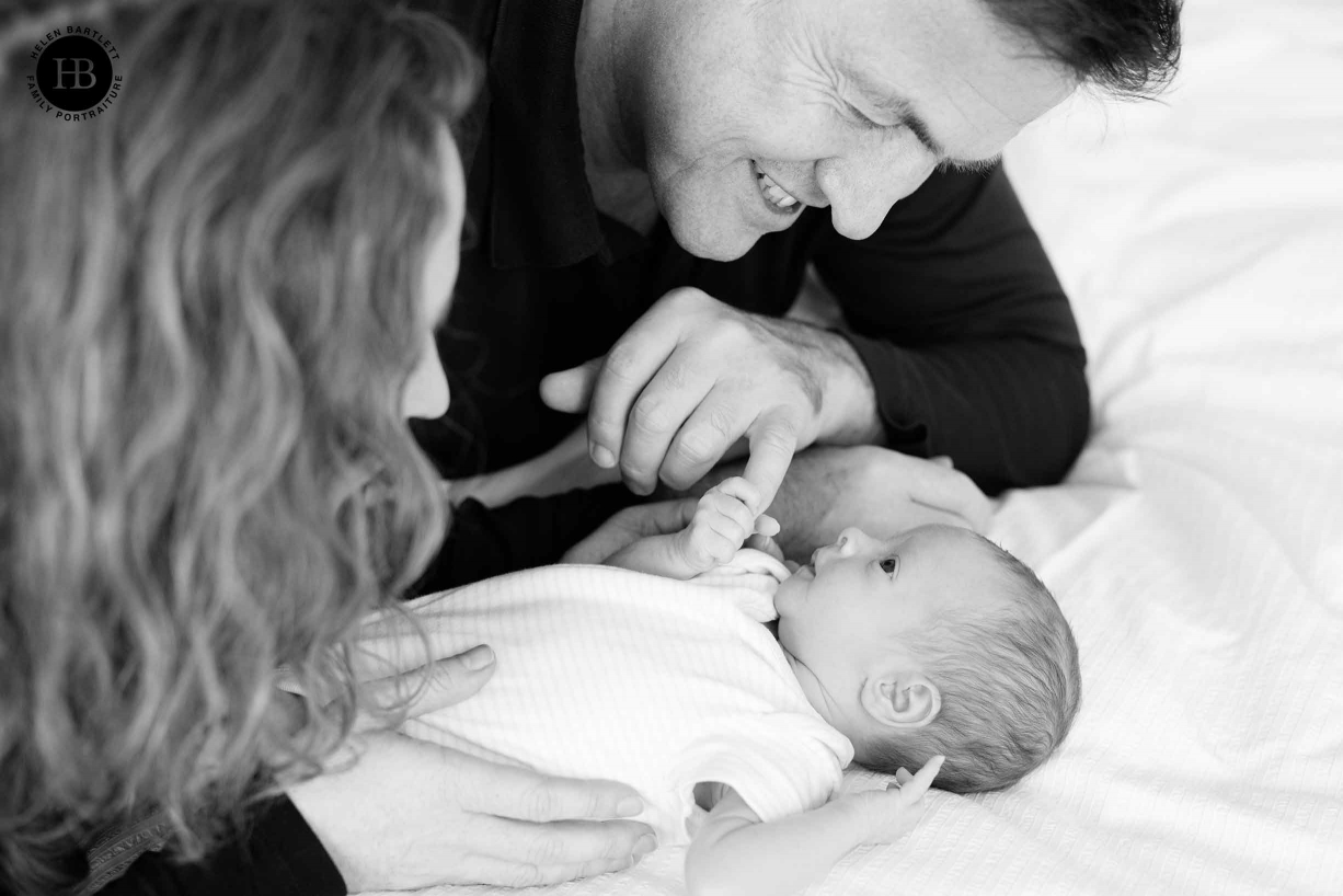 parents look at newborn baby lying on bed, baby holds father's finger