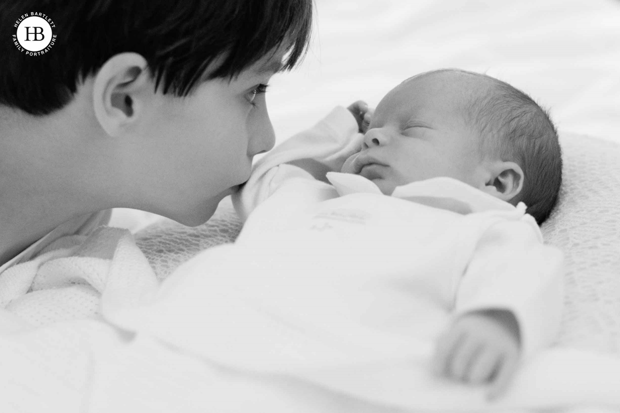 big brother kisses sleeping newborn sibling on professional photo shoot