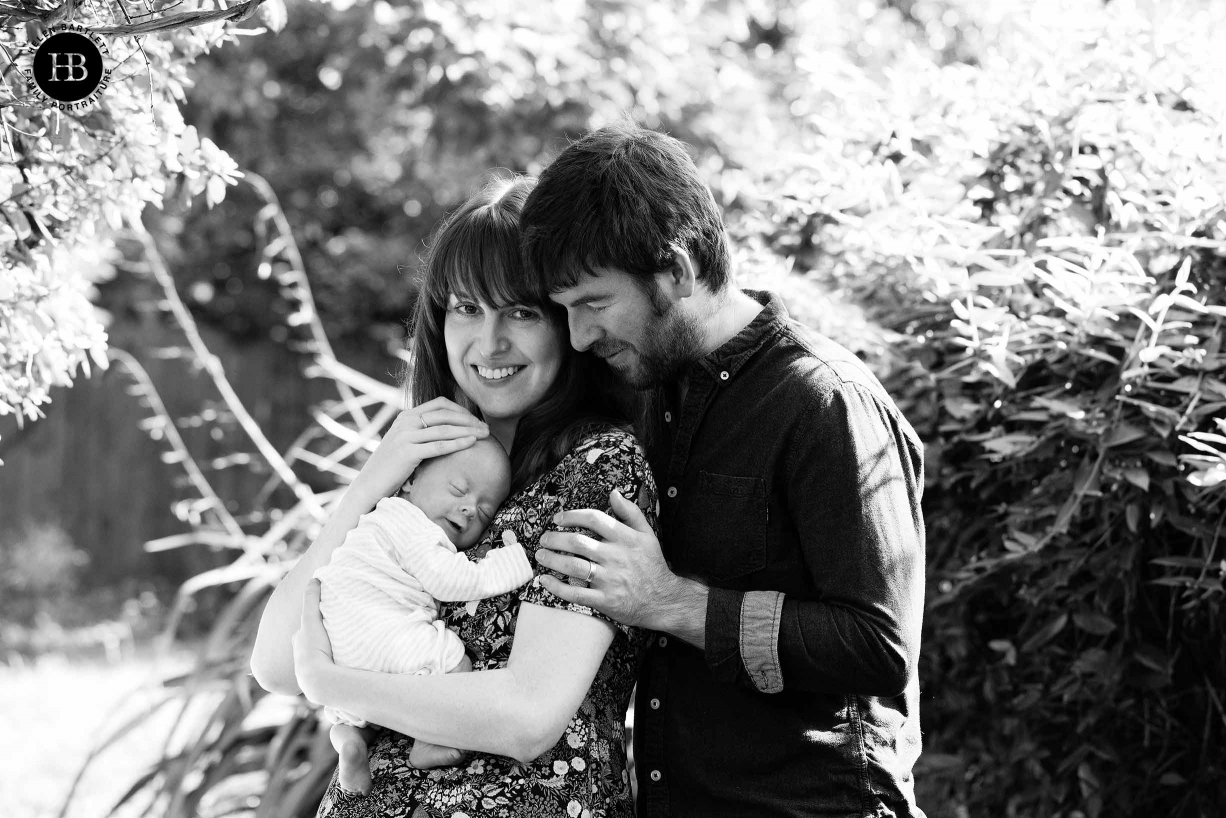 a glorious sunny day, mum and dad hold smiling newborn in the garden