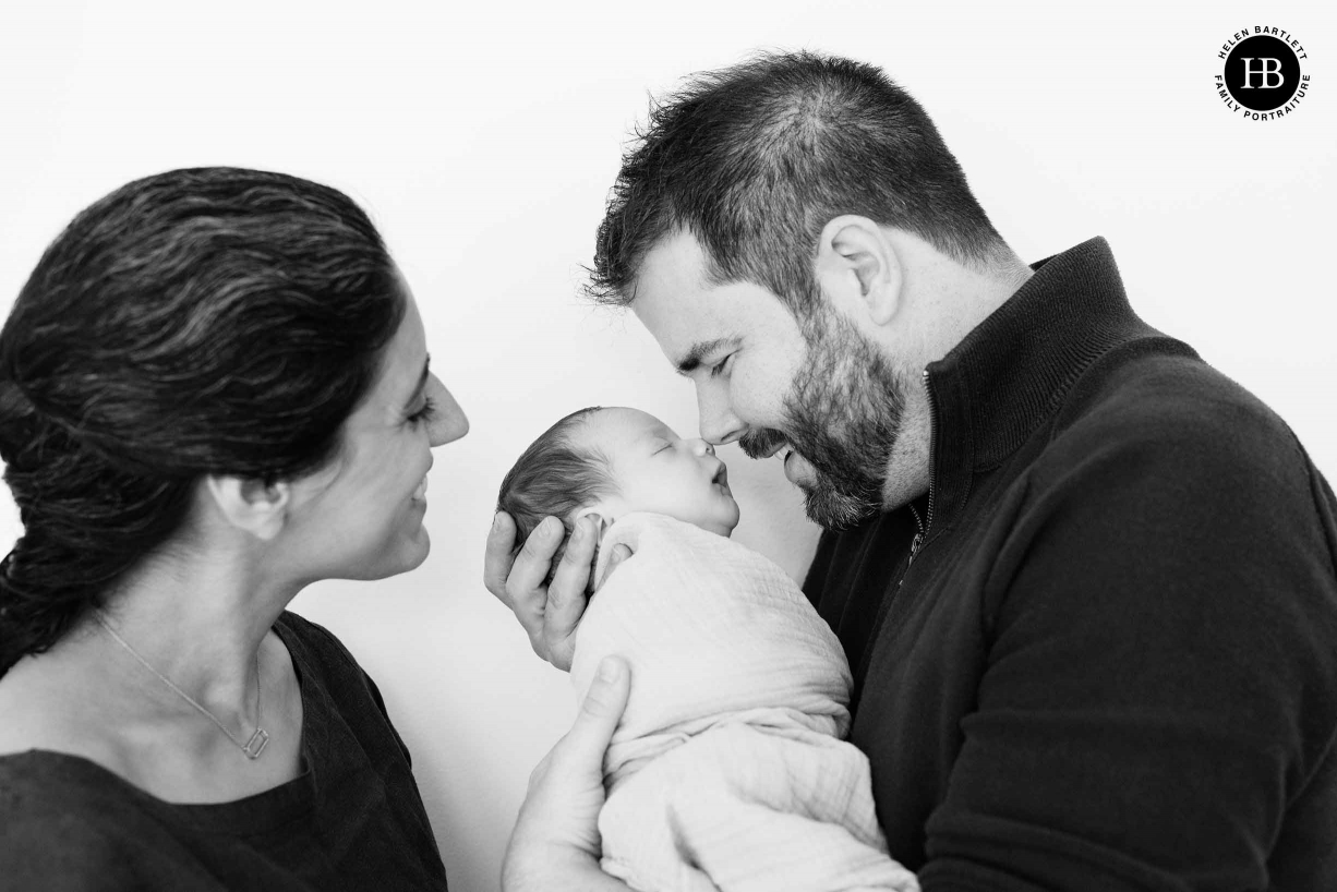 dad touches noses with baby son, mum looks on smiling