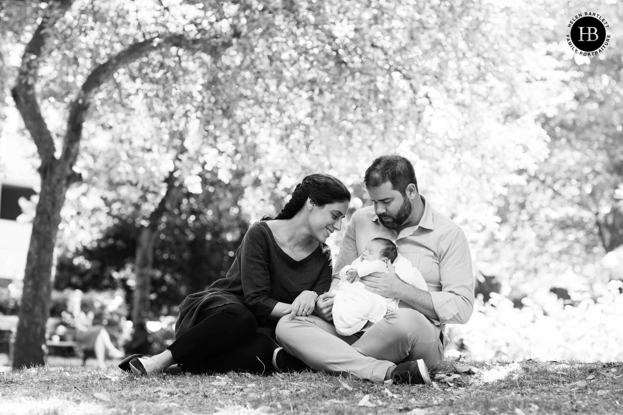 parents and newborn sit under a tree in north london park in spring