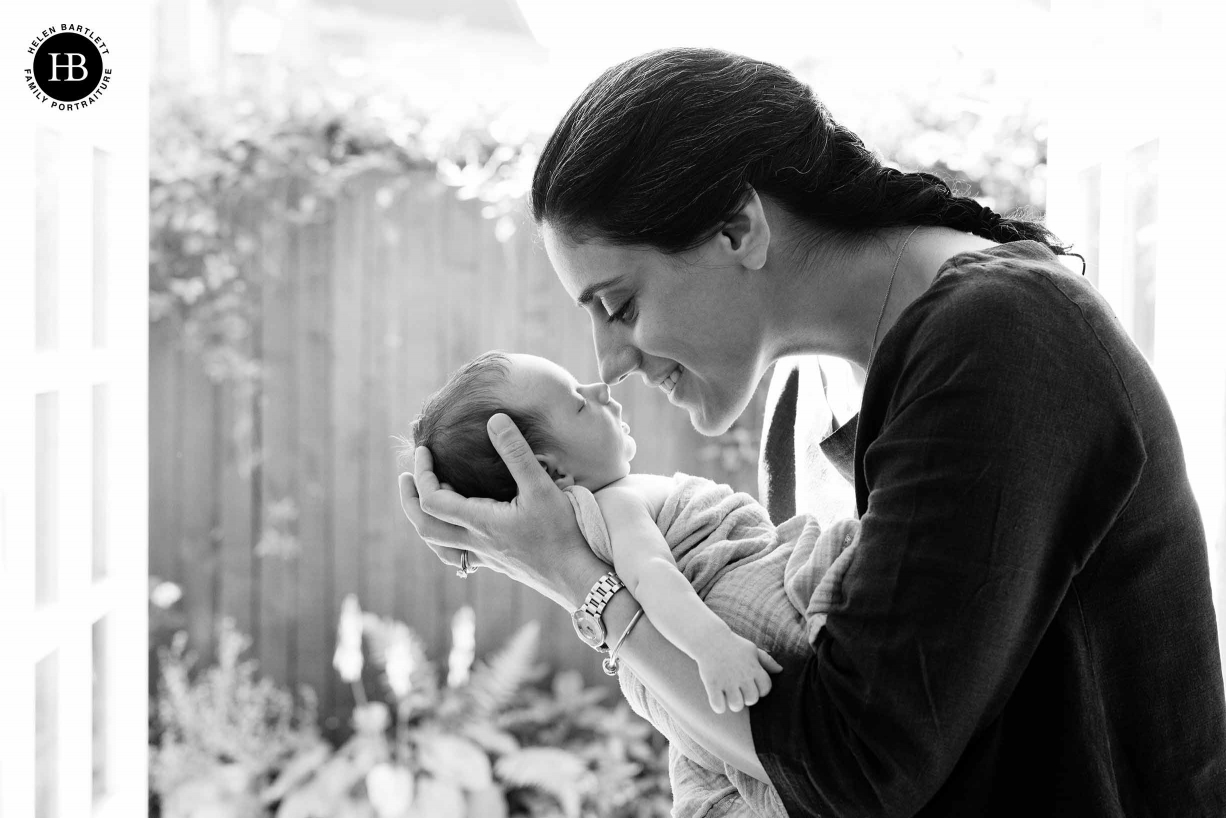 mum and newborn baby touch noses, garden in background