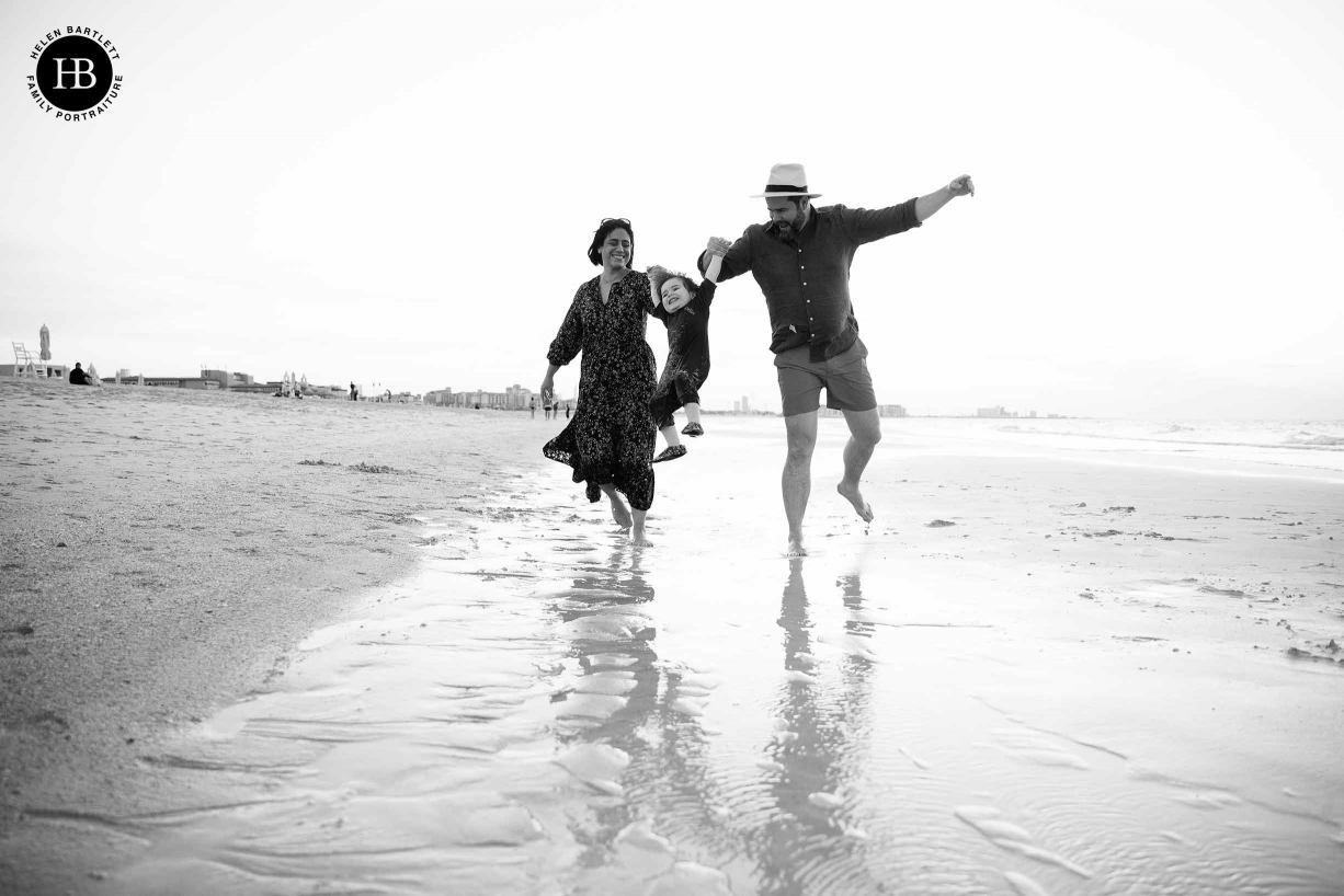 mum and dad swing little boy on the beach at sunset