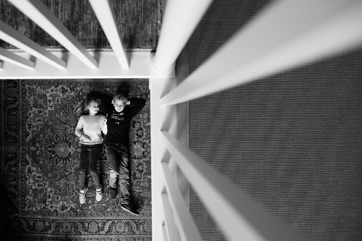 Two teenagers on a rug are framed by upstairs bannisters in this lifestyle teenage portrait by London photographer Helen Bartlett.